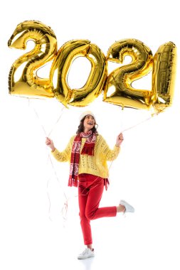 Noel Baba şapkalı ve atkılı neşeli kadın elinde 2021 numaralı balonlar ve beyaz renkli poz veriyor.