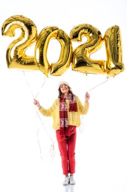 Noel Baba şapkalı ve fularlı mutlu kadın elinde balonlarla 2021 numaralı balonları beyaz üzerinde izole edilmiş olarak tutuyor.