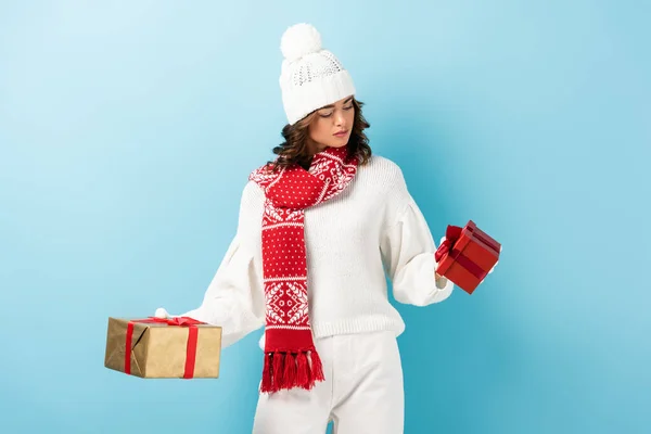 young brunette woman in winter outfit looking at presents on blue