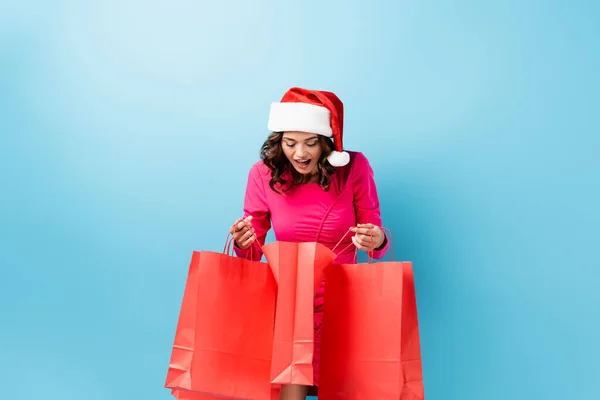 Excited Young Brunette Woman Santa Hat Looking Shopping Bags Blue — Stock Photo, Image