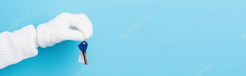 panoramic crop of woman in white glove holding key on blue
