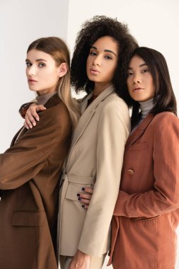 Pastel resmi giyinmiş ırklar arası genç kadınlar beyazlar üzerinde poz veriyorlar.