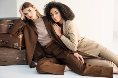 Genç manken ve Afrikalı Amerikalı kadın beyaz bavulların yanında poz veriyorlar.