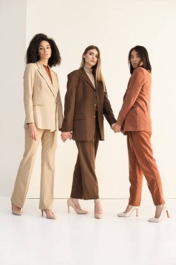 Takım elbiseli, beyazlar üzerinde poz verirken el ele tutuşan şık ırklar arası modeller.