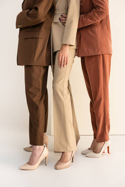 cropped view of women in formal wear and high heel shoes posing on white