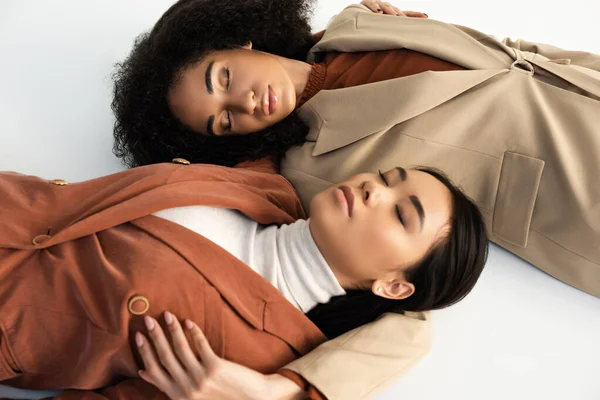 穿着时髦西服 紧闭双眼躺在白衣上的亚裔和非洲裔美国女性的头像 — 图库照片