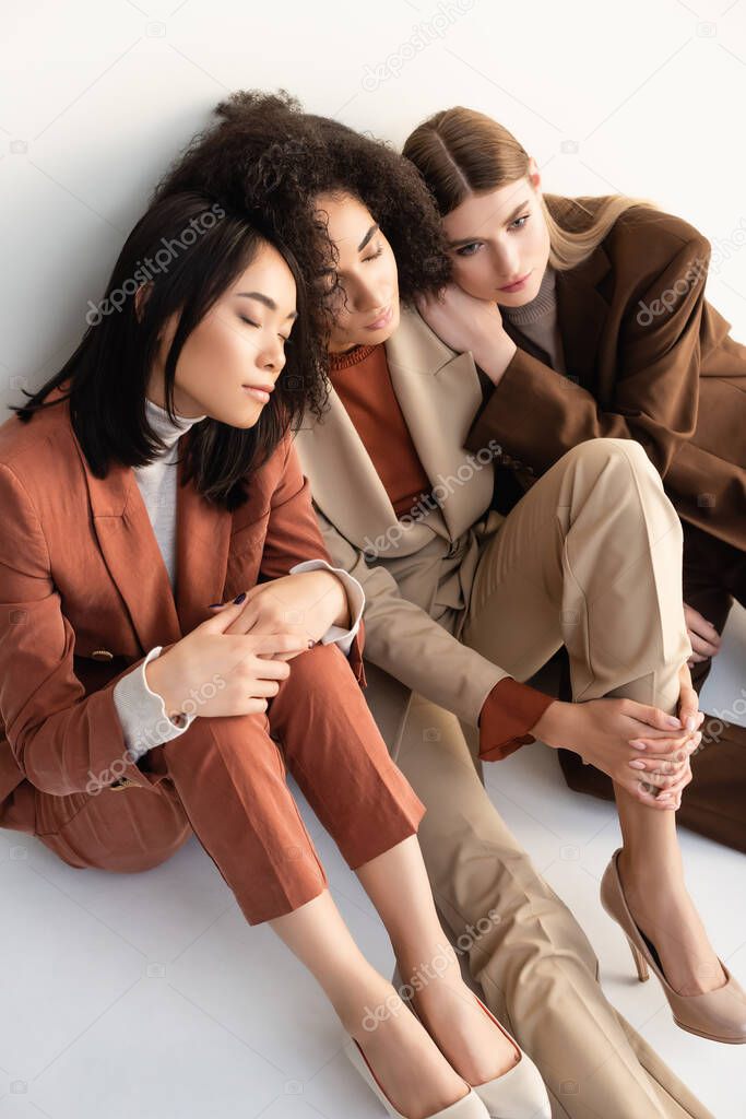 high angle view of multicultural women in trendy suits sitting on white