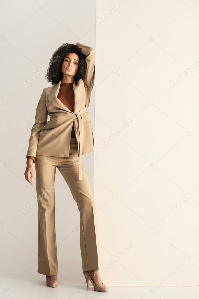 full length of curly african american woman in stylish suit posing on white