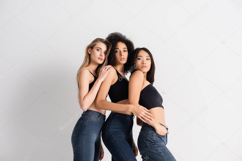 interracial women in tops and denim jeans posing on white