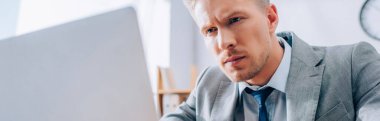 Focused businessman looking at laptop on blurred foreground in office, banner 