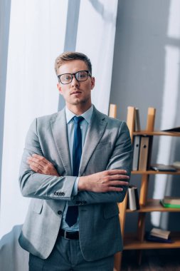 Gözlüklü ve takım elbiseli genç işadamı ofiste kameraya bakıyor. 