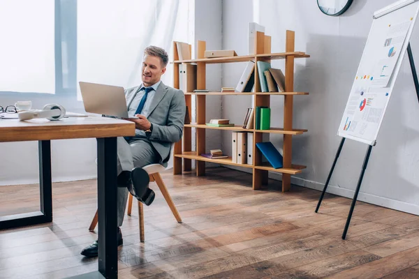 オフィスで仕事をしながらノートパソコンを使って笑顔のビジネスマン — ストック写真