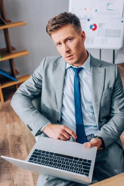 Affärsman Kostym Tittar Kameran Medan Håller Laptop Suddig Förgrund Kontor — Stockfoto