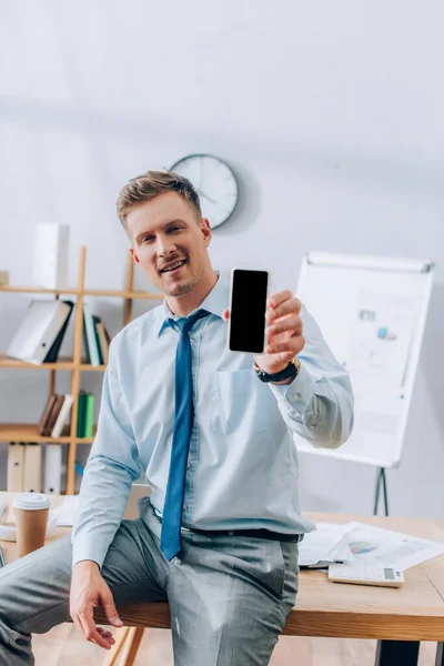 Gülümseyen Işadamı Ofisteki Bulanık Önplanda Boş Ekranlı Akıllı Telefonu Gösteriyor — Stok fotoğraf