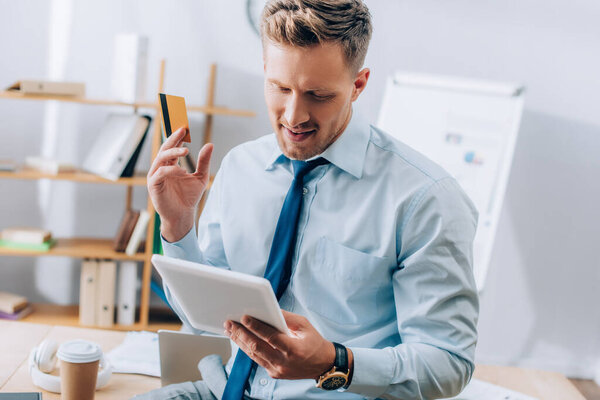 Улыбающийся бизнесмен, держащий кредитную карту при использовании цифрового планшета в офисе 