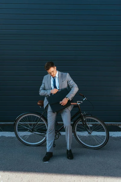Businessman with briefcase standing near bike outdoors