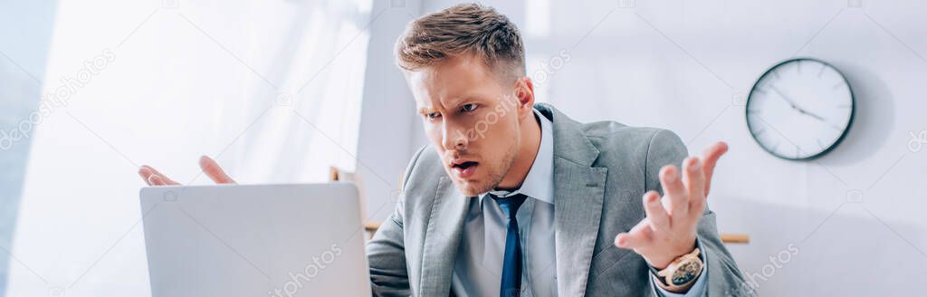 Aggressive businessman looking at laptop on blurred foreground in office, banner 