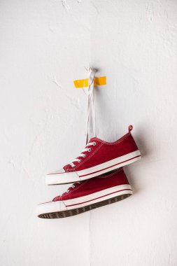 Beyaz desenli duvarın yanında ayakkabı bağcıklarına asılı kırmızı spor ayakkabılar.