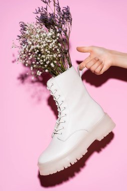 Kırpılmış pembe arka planda kır çiçekleriyle beyaz çizme tutan kadın manzarası