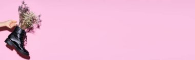 Kırpılmış pembe arka planda kır çiçekleriyle siyah çizme tutan kadın manzarası, afiş