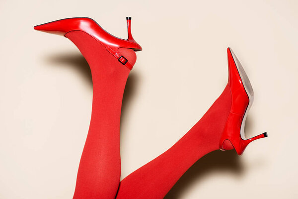 cropped view of female legs in red tights and shoes on beige background