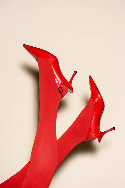 обрезанный вид женских ног в красных колготках и обуви на бежевом фоне