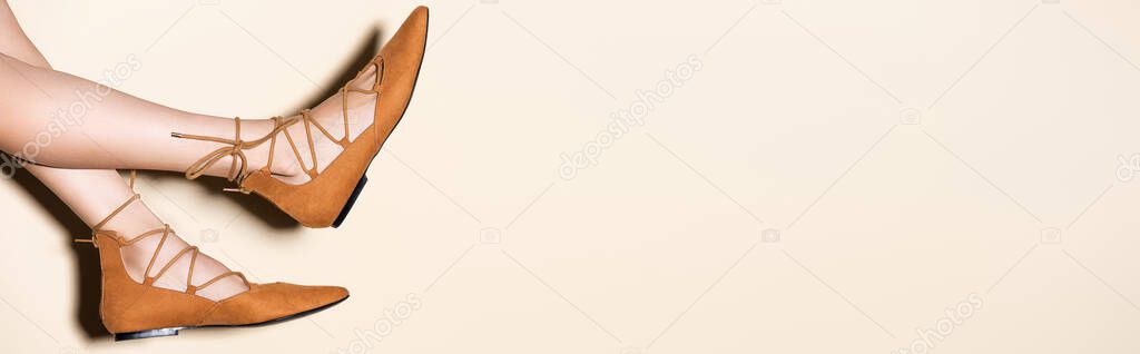 cropped view of female legs in brown suede flat shoes on beige background, banner