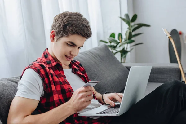 Adolescent masculin utilisant un ordinateur portable et payer par carte de crédit à la maison — Photo de stock