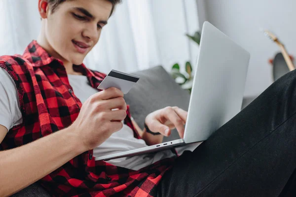 Adolescent faisant des achats en ligne avec ordinateur portable et carte de crédit à la maison — Photo de stock