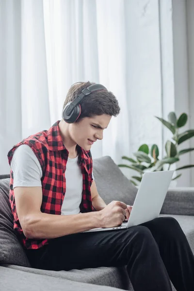 Adolescente confundido con auriculares jugando juego en el ordenador portátil - foto de stock