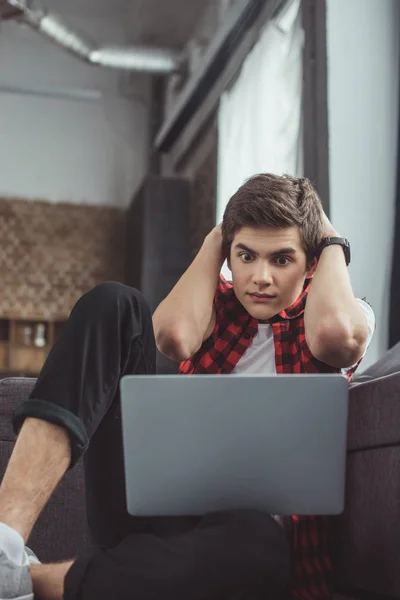 Shocked teenager looking at laptop while sitting on floor — Stock Photo