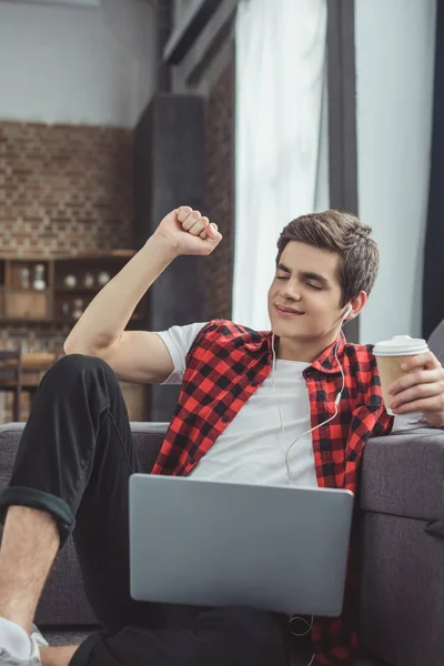 Felice adolescente con caffè per andare ad ascoltare musica con auricolari e laptop — Foto stock