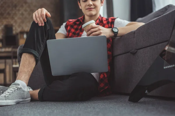 Adolescente con taza de café desechable usando el ordenador portátil - foto de stock