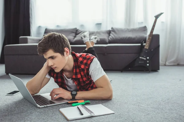 Male teenager studying with copybook and laptop while lying on floor — Stock Photo