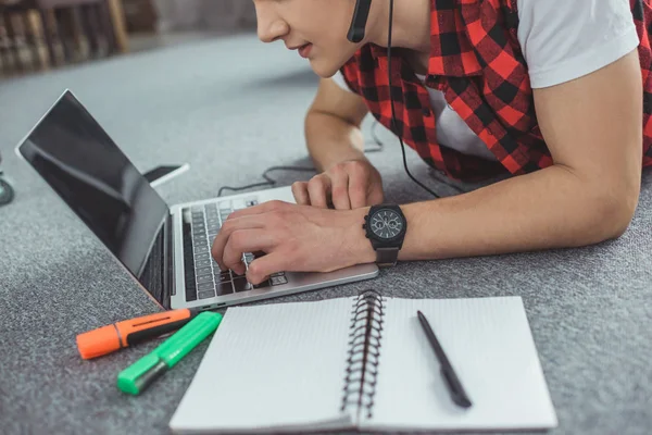 Vista parziale di adolescente che parla sullo smartphone mentre fa i compiti con il computer portatile e sdraiato sul pavimento — Foto stock