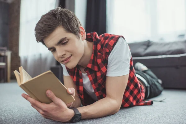 Teenager liest Buch, während er zu Hause auf dem Boden liegt — Stockfoto
