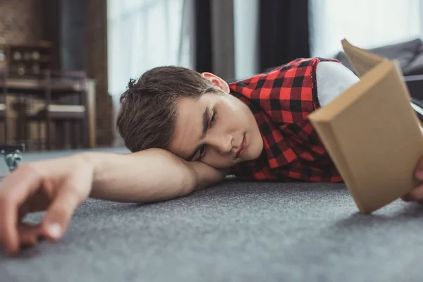 Adolescente estudiando y leyendo libro mientras está acostado en el suelo - foto de stock
