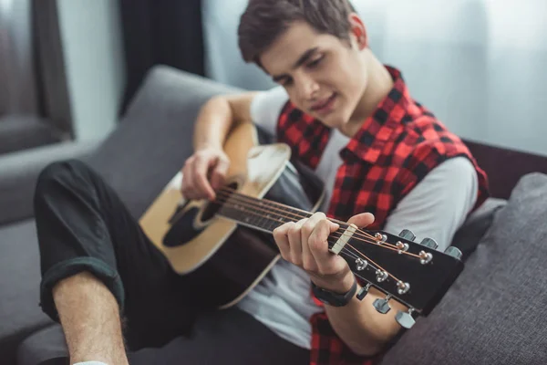 Селективное внимание подростка, играющего на акустической гитаре дома — стоковое фото