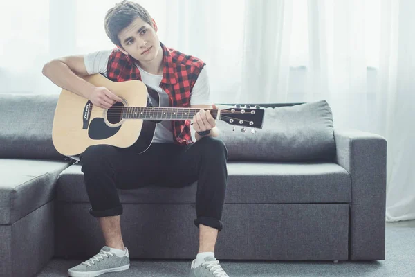 Задумчивый подросток играет на акустической гитаре дома — стоковое фото