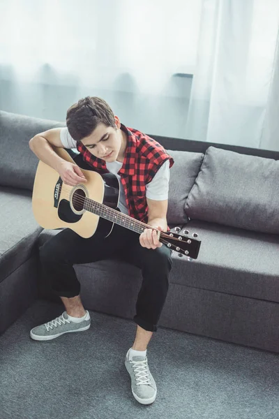 Чоловічий підліток грає на акустичній гітарі на дивані вдома — стокове фото