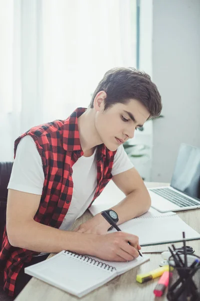 Joven estudiante masculino escribiendo tareas en la mesa - foto de stock