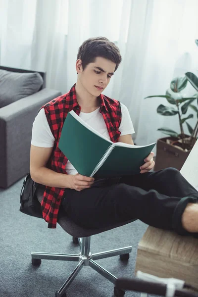 Estudiante masculino leyendo libro de texto en la mesa en casa - foto de stock