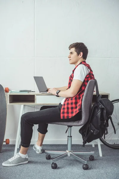 Pensativo joven estudiante haciendo la tarea con el ordenador portátil - foto de stock