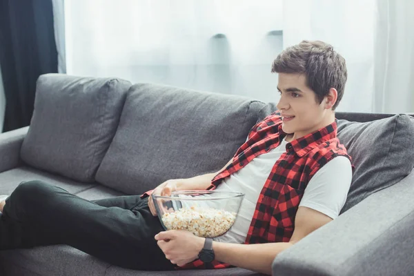 Підліток з попкорном дивиться телевізор і сидить на дивані вдома — стокове фото