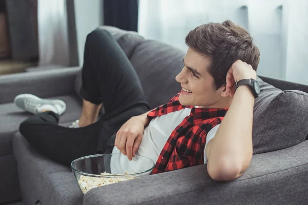 Smiling teenager with popcorn watching movie on sofa at home — Stock Photo