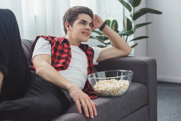 Smiling male teenager with popcorn watching movie at home — Stock Photo