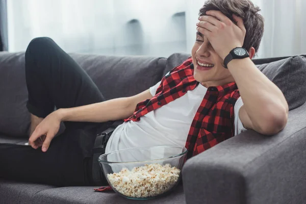 Laughing teenager with popcorn watching comedy movie at home — Stock Photo