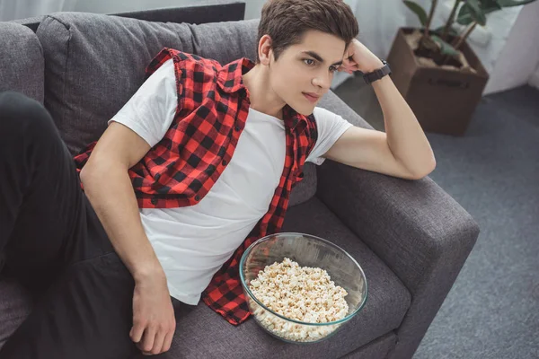 Guapo adolescente con palomitas de maíz viendo la televisión en casa - foto de stock