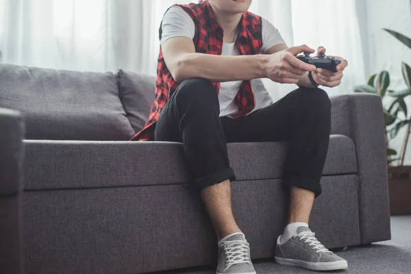 Обрезанный вид человека, играющего дома в видеоигру с джойстиком — стоковое фото