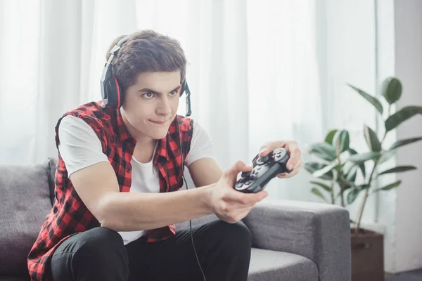 Подросток с гарнитурой играет дома в видеоигру с геймпадом — стоковое фото